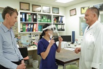 surgeon trying on a face shield in a doctor's office with biomedical engineers 