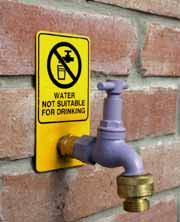 Sign – Photograph of tap on a brick wall with a yellow and black sign affixed above it. The sign states: “Water not suitable for drinking.”