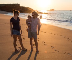Family of 3 standing on a beach as the sun sets behind them